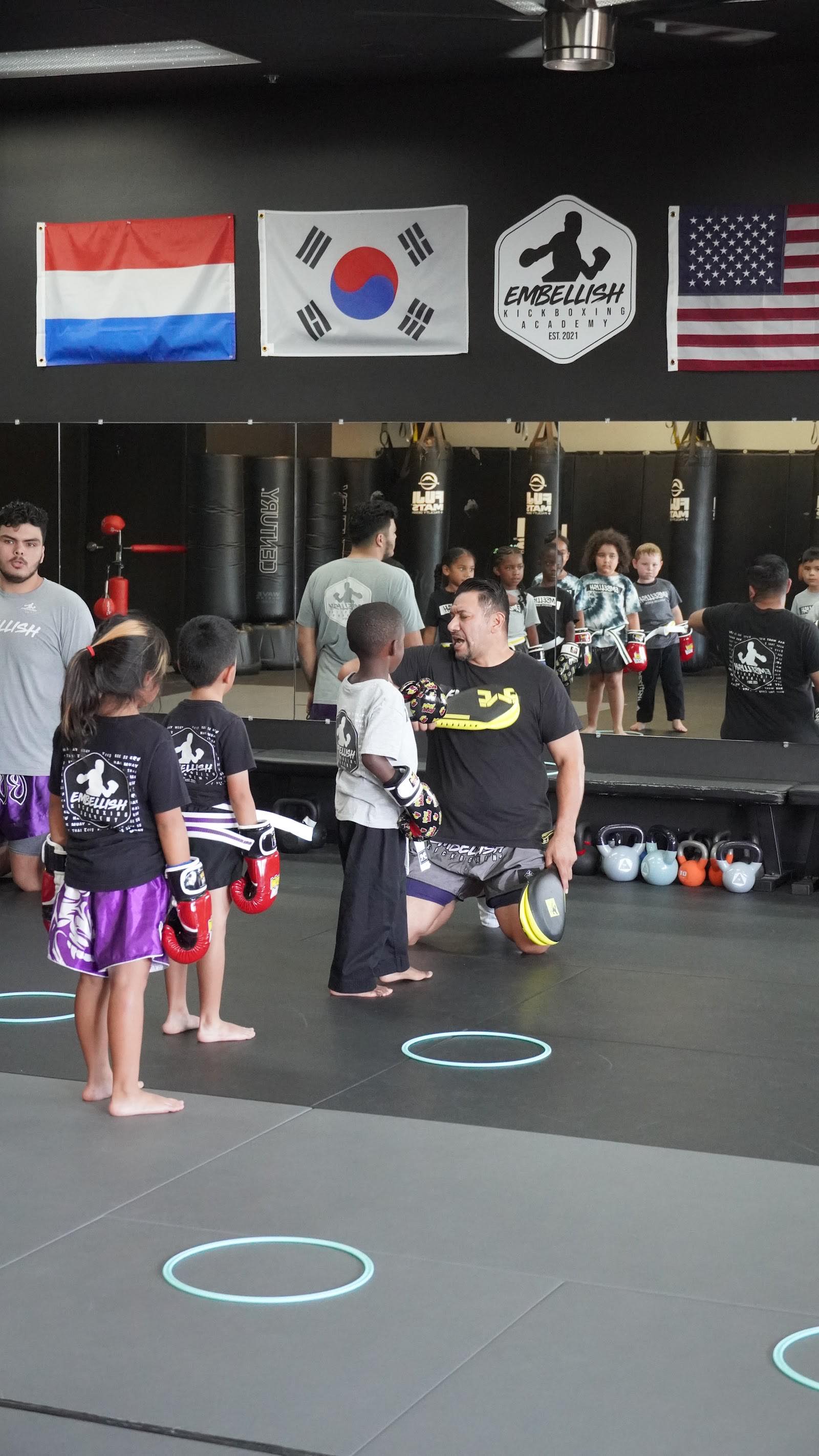 Embellish Kickboxing Academy coach kneeling to hold pads for a young student in Elk Grove.